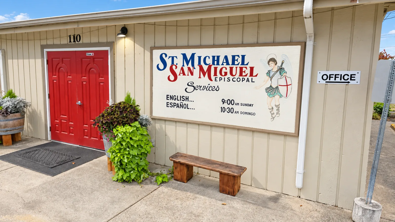 The church sign beside the brick bell tower and red doors.