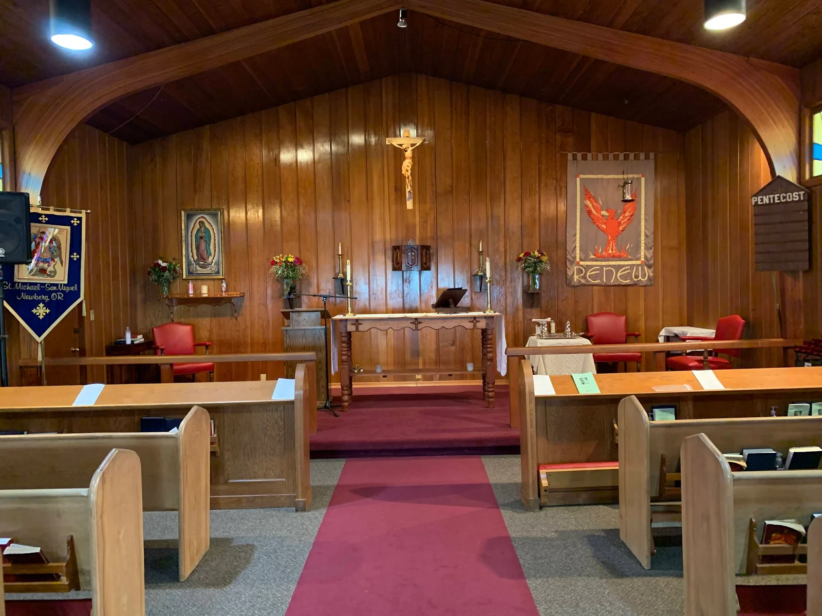 Wooden pews and a center aisle facing the altar inside St. Michael - San Miguel.